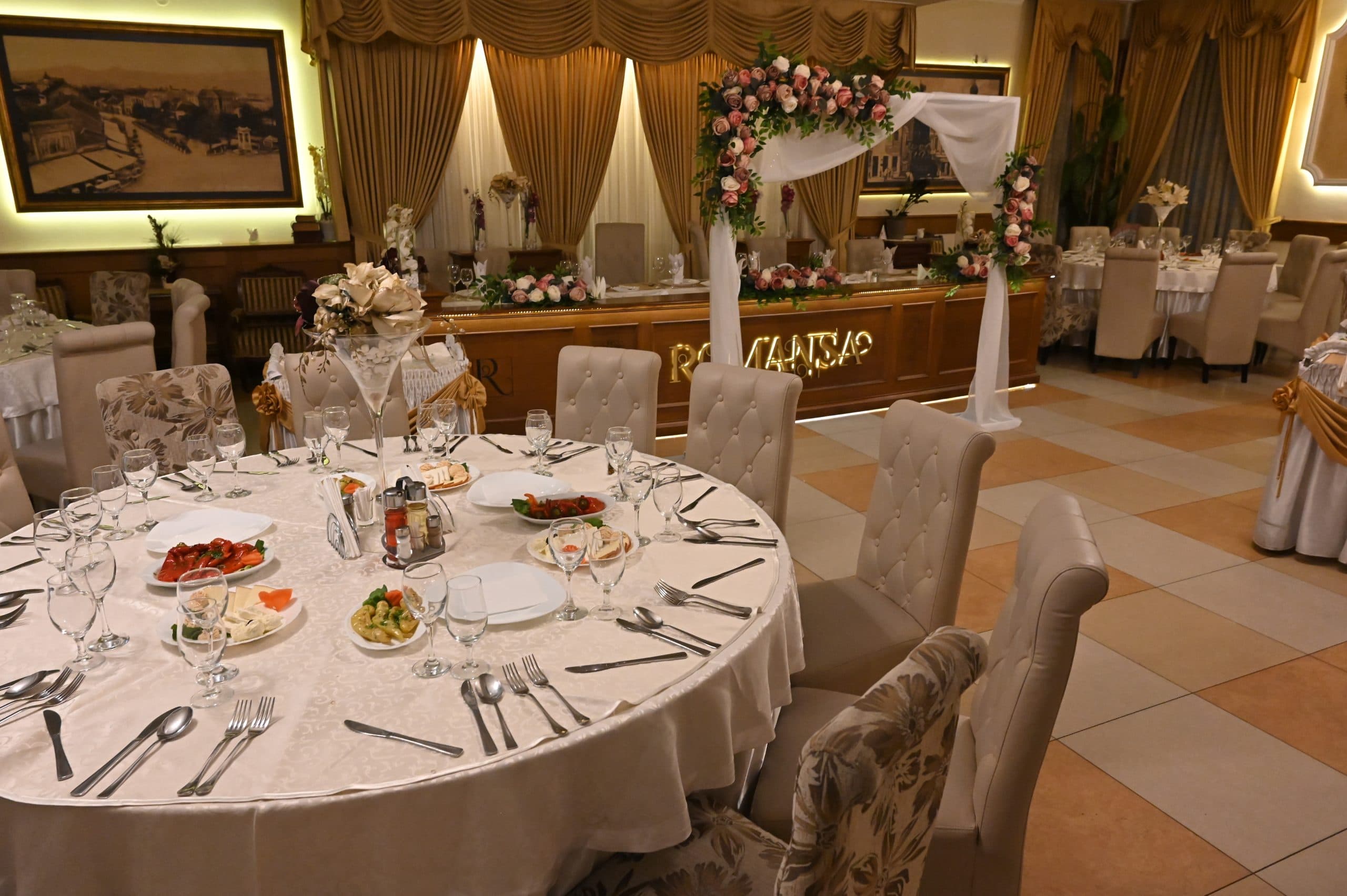 Svečano uređena sala restorana Romansa sa zlatnim zavesama i cvetnim aranžmanom, pripremljena za proslavu